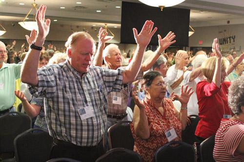 John Hotz of Russellville (left) joins Erlinda Keller of Little Rock and the rest of the crowd giving praise during the conference's opening session.
