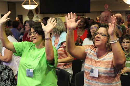 Cecelia Patton of Benton (left) and Robin Horn of Alexander raise their hands in praise during the program Aug. 3. Catholics from as far away as California attended the event.