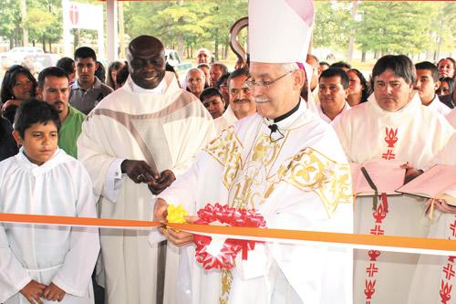 Before a throng of onlookers, Bishop Taylor cuts the ribbon outside Holy Spirit Church in Hamburg. Pastor Father Theophilus Okpara (left) then ceremoniously unlocked the front door of the new church. Arkansas Catholic photo by Dwain Hebda