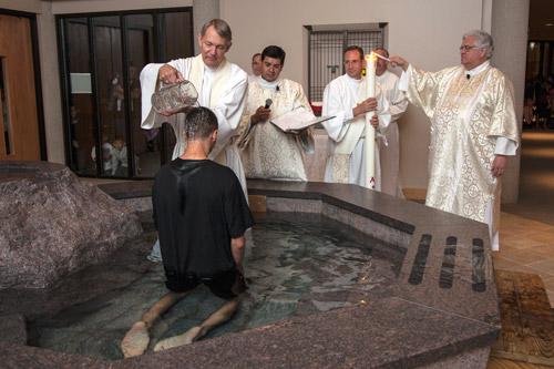 Msgr. David LeSieur, pastor of St. Vincent de Paul Church in Rogers, baptizes Justin Amaya April 19 during the Easter vigil. Assisting are Deacons Arturo Castrejon, Ronnie Hoyt and John Pate. In the background are altar server John Carney and seminarian Michael Davis. Arkansas Catholic photo by Paul Dufford
