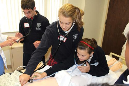 Our Lady of the Holy Souls sixth graders Elizabeth Meadors (center) and Emma Stewart Kohler use their stethoscopes on a realistic training dummy while C.J. Springer (left) awaits his turn. In a three-hour field trip to CHI St. Vincent Infirmary in Little Rock, students also learned about patient monitoring, germ containment and hospital operations. (Dwain Hebda photo)