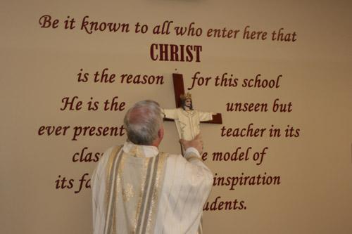 Msgr. Francis Malone hangs a new crucifix, blessed by Bishop Taylor, in the main office at Christ the King School. 