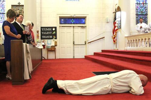 Diaconate candidate Normal McFall lies prostrate on the ground during the Litany of Supplication. His wife Laura (left) and son Samuel look on from the front row. (Dwain Hebda photo)