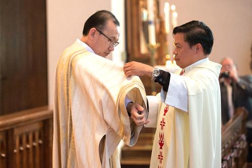 Father Jack Vu of Jonesboro assists Deacon Joseph Chan with his stole and dalmatic, signs of his new office. (Karen Schwartz photo)