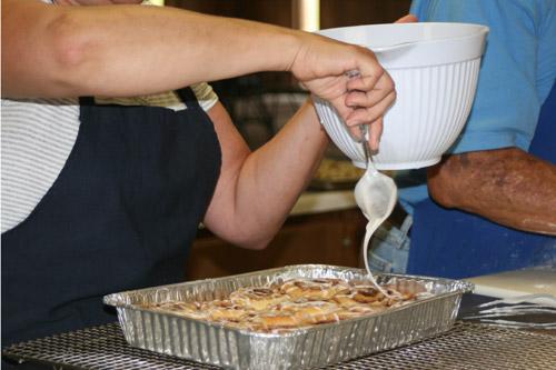 Susan Lisko coats cinnamon rolls with frosting right after being taken out of the oven. (Aprille Hanson photo) 