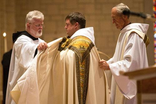 Brother Mel Stinson, OSB (left) and Father Mark Stengel, OSB, assist Father Patrick Boland with his vestments June 20 at Subiaco. (Karen Schwartz photo)