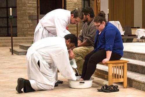 At St. Vincent de Paul Church in Rogers on Holy Thursday, associate pastor Father John Miranda assisted by Deacon Sylvestre Duran washes the feet of Carolyn Lawson after just finishing washing the feet of Josh Smith. (Paul Dufford photo)