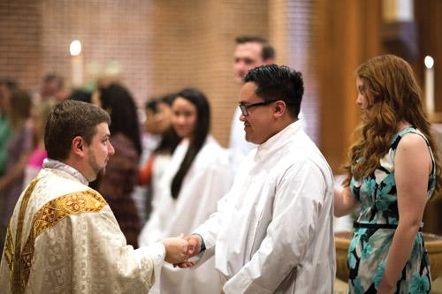 Administrator Father Andrew Hart shakes hands with Daniel Sundara during the Easter Vigil Mass at St. Thomas Aquinas University Parish in Fayetteville. Sundara, who grew up Buddhist, came into the Church through the support of his wife, Kelsey, who was also his sponsor. (Travis McAfee photo)