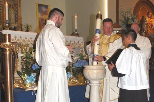 Seminarian Luke Womack looks on as pastor Father George Sanders lowers the paschal candle into the water three times during the Easter Vigil at St. Mary Church in Hot Springs.  Altar Server Dylan Nguyen holds the Missal. (Prints not available.)