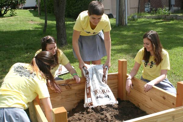 Erica Vanhaute pours soil into a new garden bed as fellow Honeybelles Catherine Dobry (left), Lauren Joseph and Cate Willis get ready to even out the dirt. (Aprille Hanson photo)