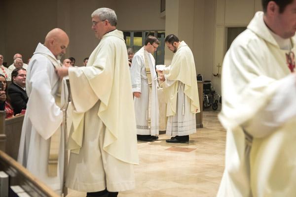Father Andrew Smith helps Father McFall (left) vest while Father Ruben Quinteros helps Father Whittington vest with the stole and chasuble during their ordination Mass. (Bob Ocken photo)