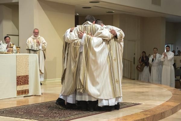 After receiving the sign of peace from the bishop and their brother priests, the five new priests for the diocese embrace each other while onlookers applaud. (Bob Ocken photo) 