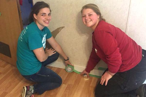 Holly Hambuchen (left) and Morgan Burke prepare to paint the trim inside a home in need of repair.