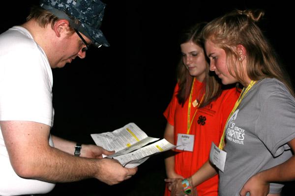 “Border patrol official” Jeff Heeter, of Christ the King Church in Little Rock, examines the paperwork of Ashley Beyer, 18 (center), of St. Michael Church in West Memphis and Bessie Sullivan, 16, of St. Stephen Church in Bentonville, before letting them cross into “Mexico.” (Aprille Hanson photo)