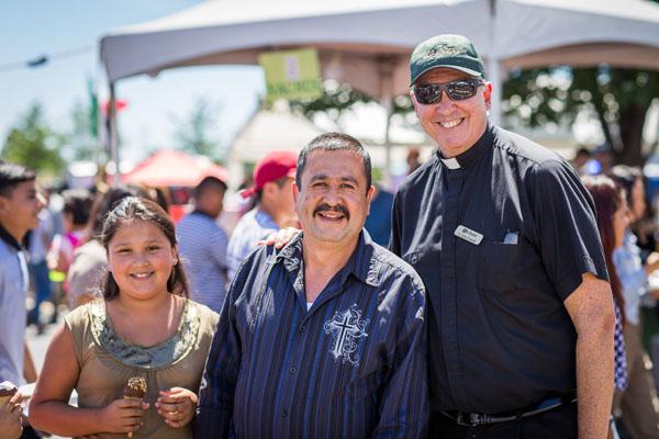 Brisa and Martin Ramirez pause for a picture with pastor Father John Connell, a proud promoter of Summerfest as an opportunity to bring together his diverse flock. (Travis McAfee photo) 