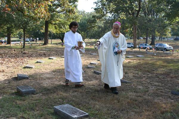 Bishop Taylor blesses the priests’ graves at Calvary Cemetery during the rosary procession on All Souls Day, Nov. 2, with assistance from John Marconi, who is discerning a call to religious life. (Aprille Hanson photo)