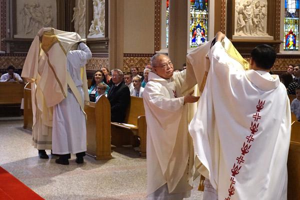 Deacons Jeff Hebert (left) and Tuyen Do are invested with the liturgical vestments of a deacon. Deacon Dominic Do (left) and Father Jack Vu vest Deacon Do.  (Aprille Hanson photo)