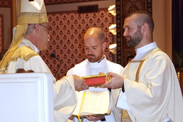 Bishop Taylor presents Deacon Jeff Hebert with the Book of Gospels as seminarian Patrick Friend assists.  (Aprille Hanson photo)