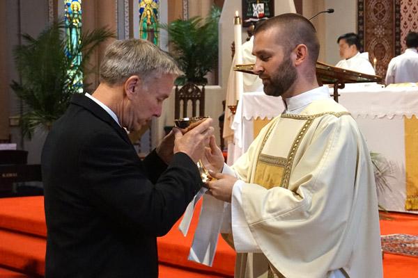 Deacon Jeff Hebert serves communion to his father, Richard Hebert, of Houston, Texas. (Aprille Hanson photo)