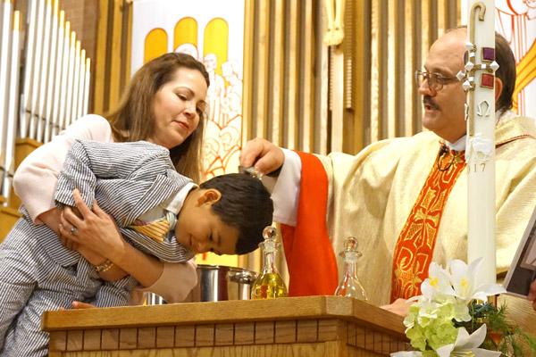 Father Norbert Rappold, pastor at St. Peter the Fisherman Church in Mountain Home, baptizes Alexander Chafin, 6, while his godmother Joanna Hill holds him up during Easter Vigil Mass April 15. (Aprille Hanson photo)