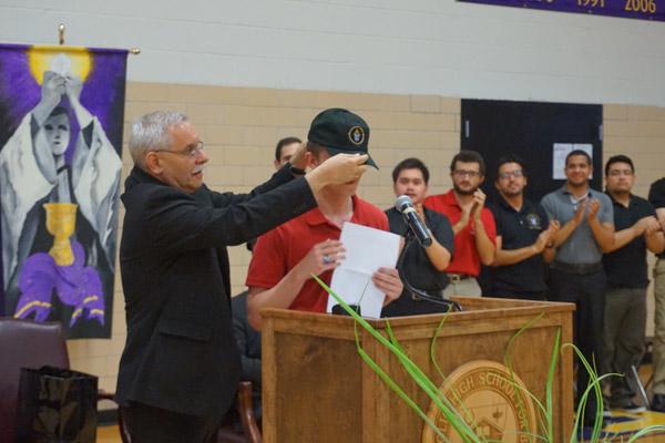 Bishop Taylor places a ball cap with a diocesan logo on Aubrey Volpert, a Catholic High graduate, who will be a seminarian in the fall. (Aprille Hanson photo)