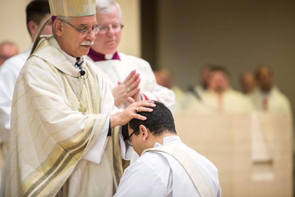 Bishop Anthony B. Taylor lays his hands on Father Ramsés Mendieta, to receive the strength of the Holy Spirit, as Msgr. Francis Malone, pastor at Christ the King Church, looks on. (Travis McAfee photo)