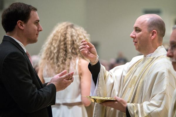 Father William Burmester gives out Communion at his ordination May 27. He said seeing familiar faces in the Communion line was a special moment during the Mass. (Travis McAfee photo)