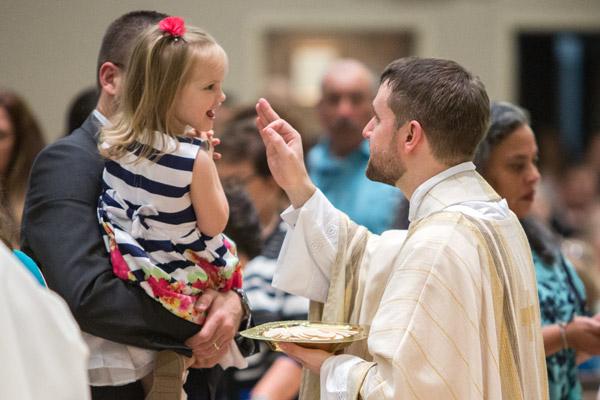 Father Stephen Hart blesses a young girl during communion. He said his priestly ordination was the “the beginning of the fulfillment of a calling.” (Travis McAfee photo)