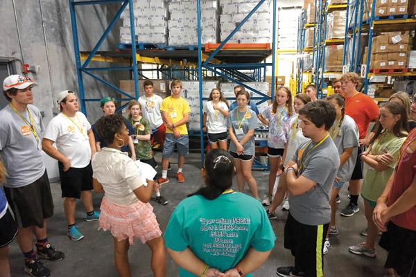 An Arkansas Foodbank staff member explains to teens attending the Catholic Charities Summer Institute how the packages they’d fill July 27 would benefit people in need. Teens attending C2SI work in service projects throughout the week. (Aprille Hanson photo)
