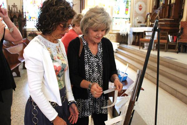 Lynn Pellegrino (left) and Denise Steinhaus of St. Mary of the Springs Church in Hot Springs tie prayer intentions to a frame before the Sept. 30 Mass. (Dwain Hebda photo)