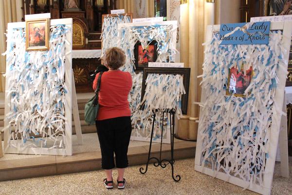 Christy Miller of Our Lady of the Springs Church in Hot Springs takes a photo of panels bearing hundreds of prayer intentions to Mary Undoer of Knots. (Dwain Hebda photo)