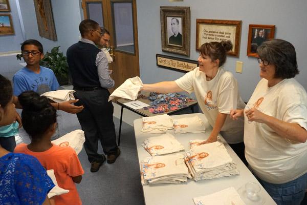 Our Lady of Fatima office manager Lori Hinojosa (left) and parish volunteer Cecelia Patton pass out Our Lady of Fatima anniversary shirts at the reception following Mass Oct. 13. (Aprille Hanson)