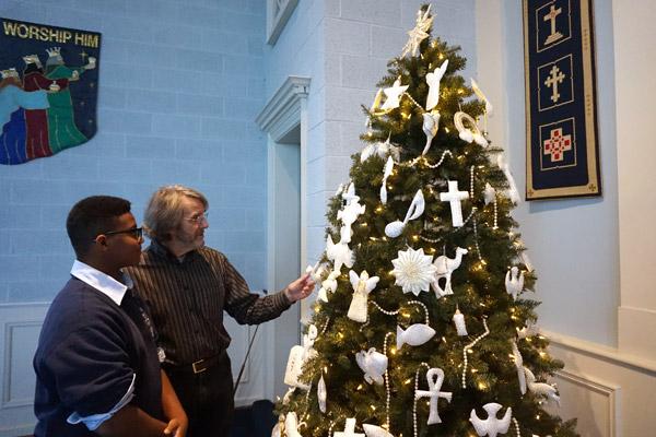 Ruskin Falls, pastor of Pulaski Heights Presbyterian Church in Little Rock, talks to his son Neil, 14, an eighth-grade student at Our Lady of the Holy Souls School, about the significance of ornaments on the Chrismon tree. (Aprille Hanson photo)