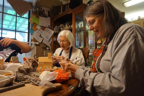 Jean Leffler (right) smiles while constructing a marshmellow snowman to put in a yard of one of the Christmas cookie houses, while Nancy Frevert works on her church. (Aprille Hanson photo)