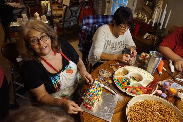 Retha Fausett (left) shows off her Christmas cookie house while Janis Garrett works on a marshmallow snowman for her house.  (Aprille Hanson photo)