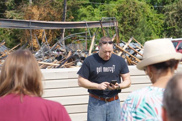 Lee Wilbur, vice president of the Arkansas Pregnancy Resource Center board of directors, reads the rosary mysteries from his phone, leading the prayers in front of the burned center. (Aprille Hanson photo)