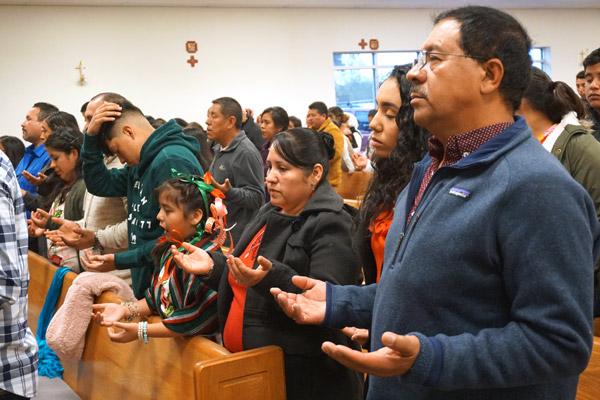 Hector Mondragon (right) and others pray the Our Father during the Dec. 8 Mass. (Malea Hargett photo)