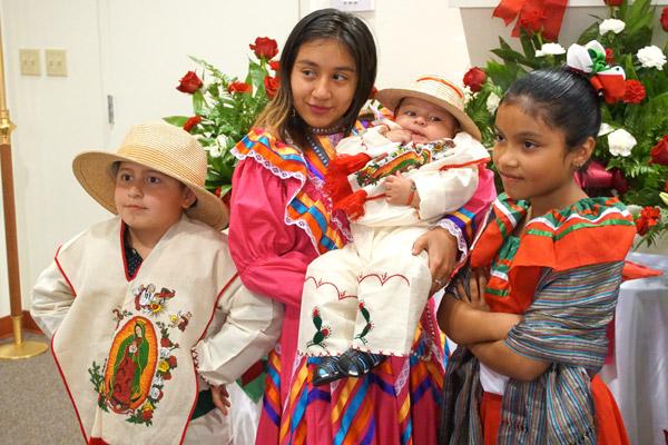 Siblings Brandon Cuellar (left), Michel Cuellar, baby Emanuel Cuellar and Pilar Fernandez pose for a family photo in front of the display of Our Lady of Guadalupe. (Malea Hargett photo)