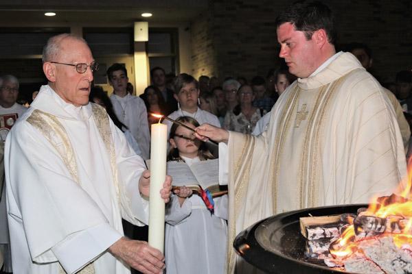 Pastor Father Tony Robbins lights the Paschal candle held by Deacon Richard Papini in photo at right as they stand next to the Holy Saturday Easter fire, April 20 at St. Joseph Church in Conway. (Photo not for sale)
