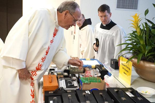 Deacon Tom Pohlmeier (left) searches for his holy oils to bring back to St. Joseph Church in Paris, as Father Paul McCambridge, FSSP, of Cabot moves closer to begin his search. Following the Chrism Mass April 15, priests and deacons pick up their containers of oils for the year. (Aprille Hanson photo)