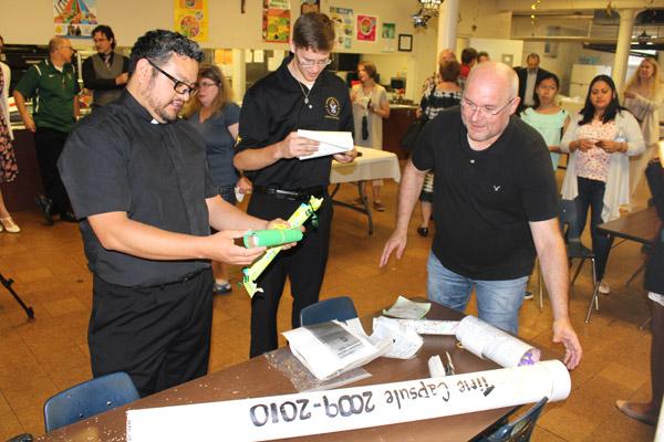 St. Edward pastor Father Juan Manjarrez (left) and diocesan seminarian John Paul Hartnedy, a St. Edward School graduate, inspect the contents of a 2010 school time capsule with Scott Sparks after the alumni Mass May 19. (Dwain Hebda photo)