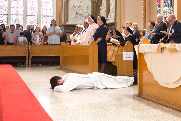 Jon Miskin lays prostrate as his family watches and the congregation sings the Litany of the Saints. (Bob Ocken photo)