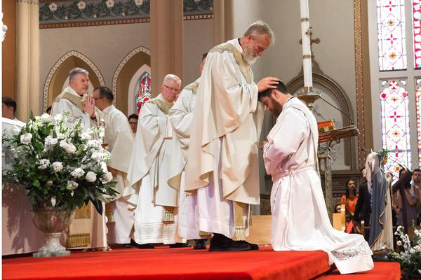 As a sign of unity among the priests, Msgr. Scott Friend and other priests present lay their hands on elect Jon Miskin. (Bob Ocken photo)
