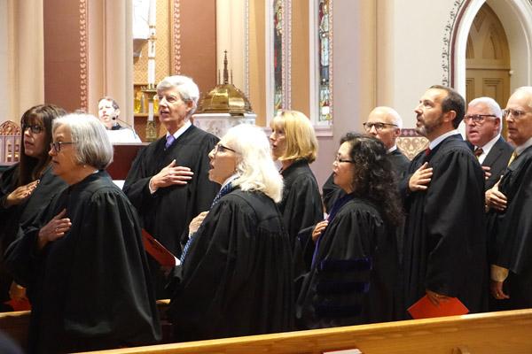 Judges salute the American flag while singing the Star Spangled Banner ahead of the 25th annual Red Mass at the Cathedral of St. Andrew in Little Rock on Oct. 4, hosted by the St. Thomas More Society. Pictured are (left to right): Stephanie Casady, Saline County District judge; Susan Weber Wright, Federal District judge; Wayne Gruber, Pulaski County District judge; Mary McGowan, Sixth Judicial Circuit judge; Rita Gruber, chief justice of the Arkansas Court of Appeals; Jessie Wallace Burchfield, Associate Dean of the William H. Bowen School of Law in Little Rock; Milas “Butch” Hale, Sherwood district judge; Andy Gill, District Court judge of Perry County; Paul Keith Arkansas Bar Association president elect; and Chaney Taylor, Batesville District Court judge. (Aprille Hanson photo)