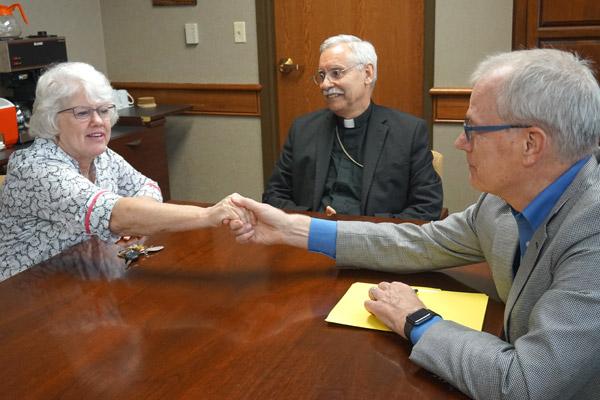 After 40 years of ministering from the diocese, Little Rock Scripture Study was sold to longtime partner Liturgical Press. Cackie Upchurch (left), retiring director of LRSS, shakes hands June 27 with Peter Dwyer, director of Liturgical Press, after he and Bishop Anthony B. Taylor signed papers transferring ownership. (Aprille Hanson, Arkansas Catholic file) 