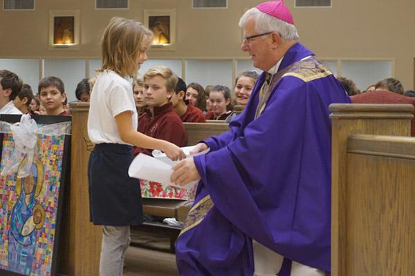 Second-grader Joanie Webb gives her letter to Bishop-elect Malone after sharing her best advice for him as bishop. He received a spiritual bouquet, letters and artwork from students at Christ the King School. (Aprille Hanson photo) 