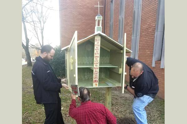 Father Josh Stengel (left) and two parishioners work on getting the little church “sharing box” installed outside Our Lady of Good Counsel Church in Little Rock in November 2018. (File photo, courtesy Our Lady of Good Counsel Church)