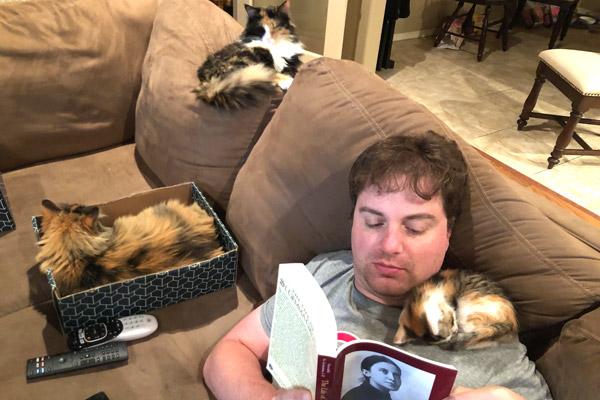 Brant Law reads with his cats at his Alma home in the summer of 2020. Law’s first book “God Saw That It Was Good: A Safari Through Salvation History” details stories of animals in the Bible, in the lives of saints and also in his personal life. (Courtesy Brant Law)