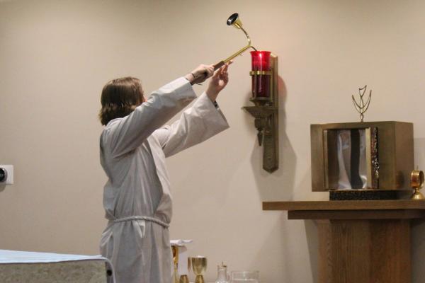 An altar server at St. Jude the Apostle Church in Jacksonville lights the sanctuary lamp beside the tabernacle during the Gloria hymn at the Easter vigil Mass March 30. (Katie Zakrzewski)