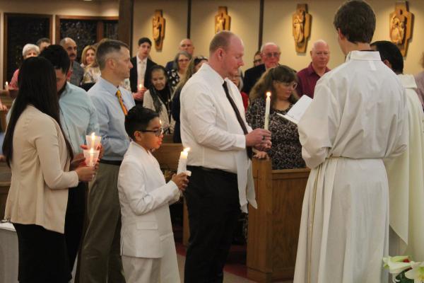 Dominick Elias Santana, a young boy and elect (center left) and Timothy James Garvin, another elect (center) light their baptismal candles after being baptized during Easter Vigil at St. Jude the Apostle Church in Jacksonville March 30. (Katie Zakrzewski)

